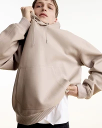 Close-up portrait of a male model wearing a beige hooded sweatshirt against a white seamless background for Dior Men.
