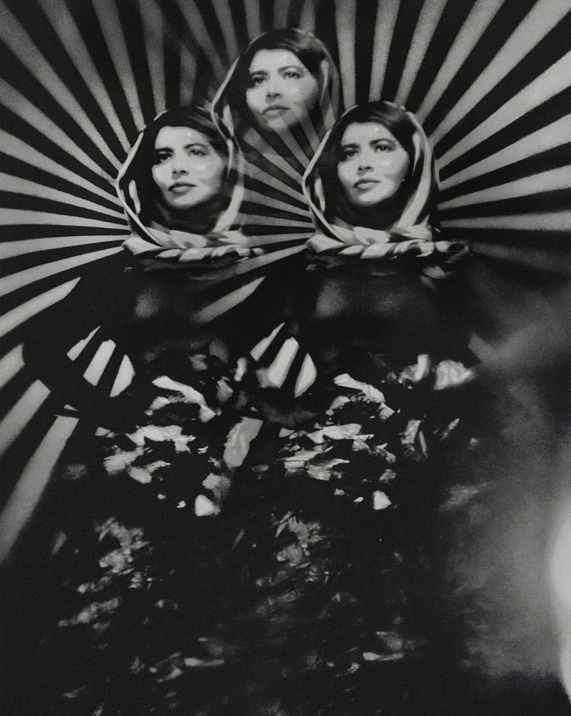 Monochrome portrait with three superimposed images of a woman wearing a headscarf against a radiating black and white striped background.