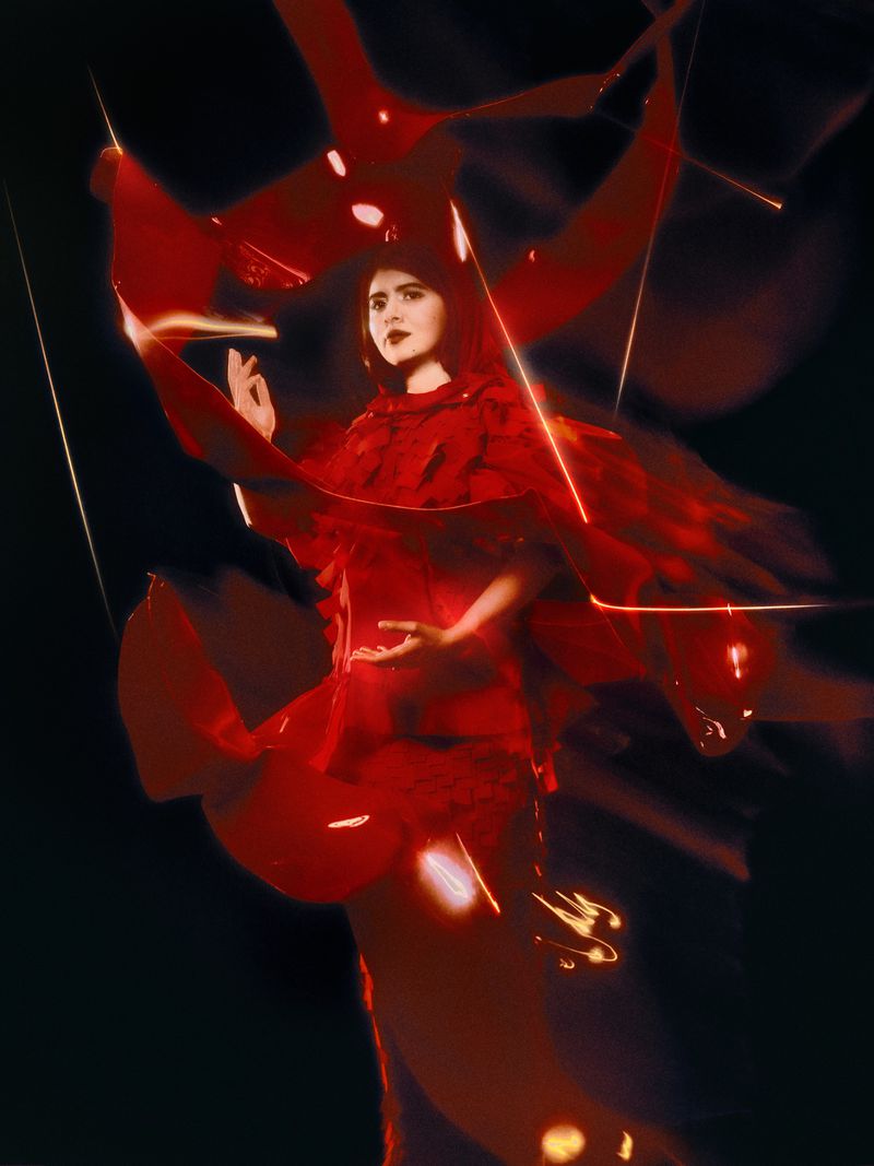 Portrait of a woman in red dress and shawl, set against a dark background, illuminated by artistic lighting in a studio setting.
