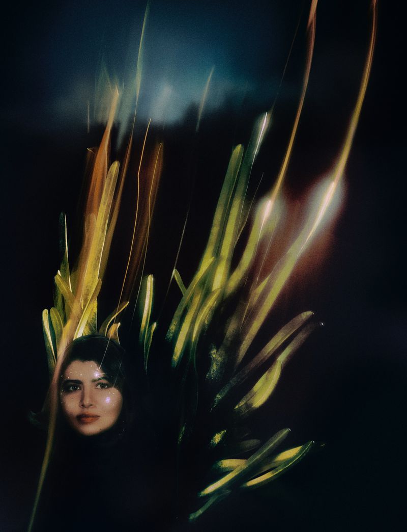 Portrait of an adult female in a dark indoor environment, illuminated by abstract light trails and foreground foliage.