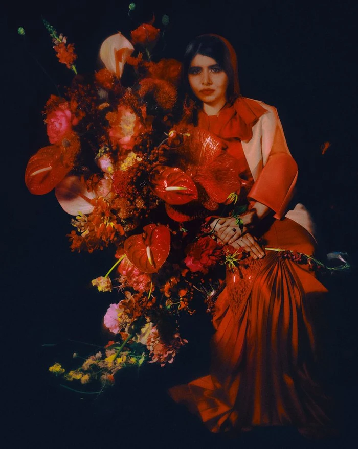 Malala Yousafzai seated beside an extravagant arrangement of red and orange flowers in a striking editorial portrait for British GQ.