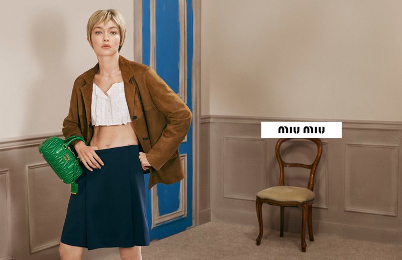 Gigi Hadid wearing a brown blazer holding a green quilted handbag in a Miu Miu campaign
