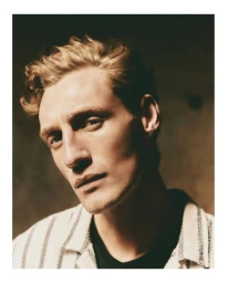 Close-up portrait of a male model with blond hair wearing a striped shirt and dark t-shirt against a dark background