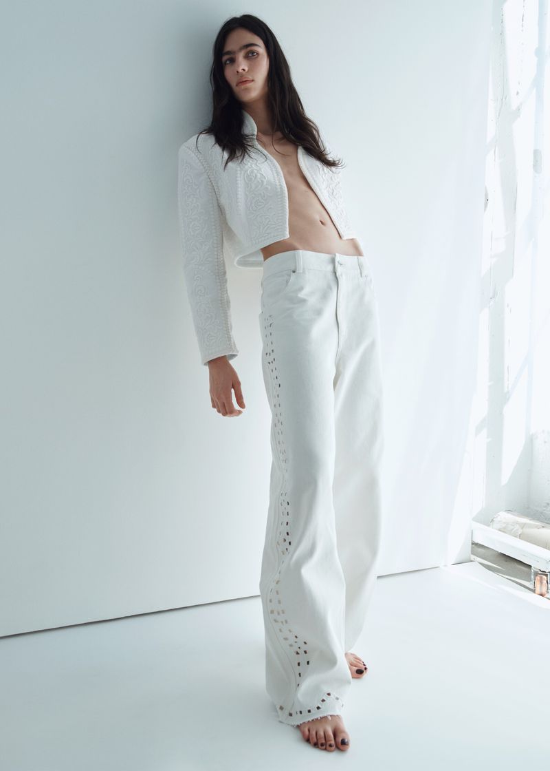 Model Loli Bahia leaning against a white studio wall in white jacket and trousers for H&M S/S 2026 campaign