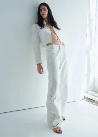 Model Loli Bahia leaning against a white studio wall in white jacket and trousers for H&M S/S 2026 campaign