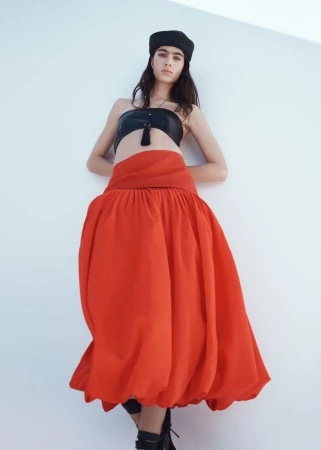 Model Loli Bahia wearing a black bandeau top and long red skirt against a white studio background for H&M S/S 2026