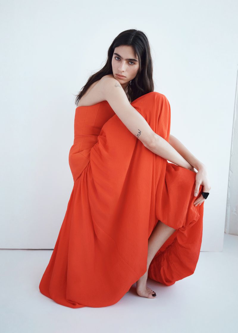 Model Loli Bahia wearing a vibrant red dress in a minimalist studio setting for H&M S/S 2026 campaign