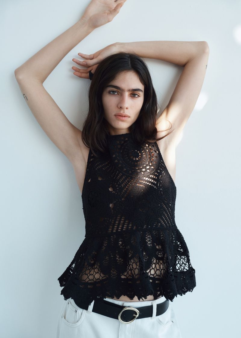 Model Loli Bahia posing in a black lace halter top and white jeans against a plain white background for H&M.