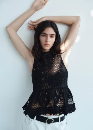Model Loli Bahia posing in a black lace halter top and white jeans against a plain white background for H&M.
