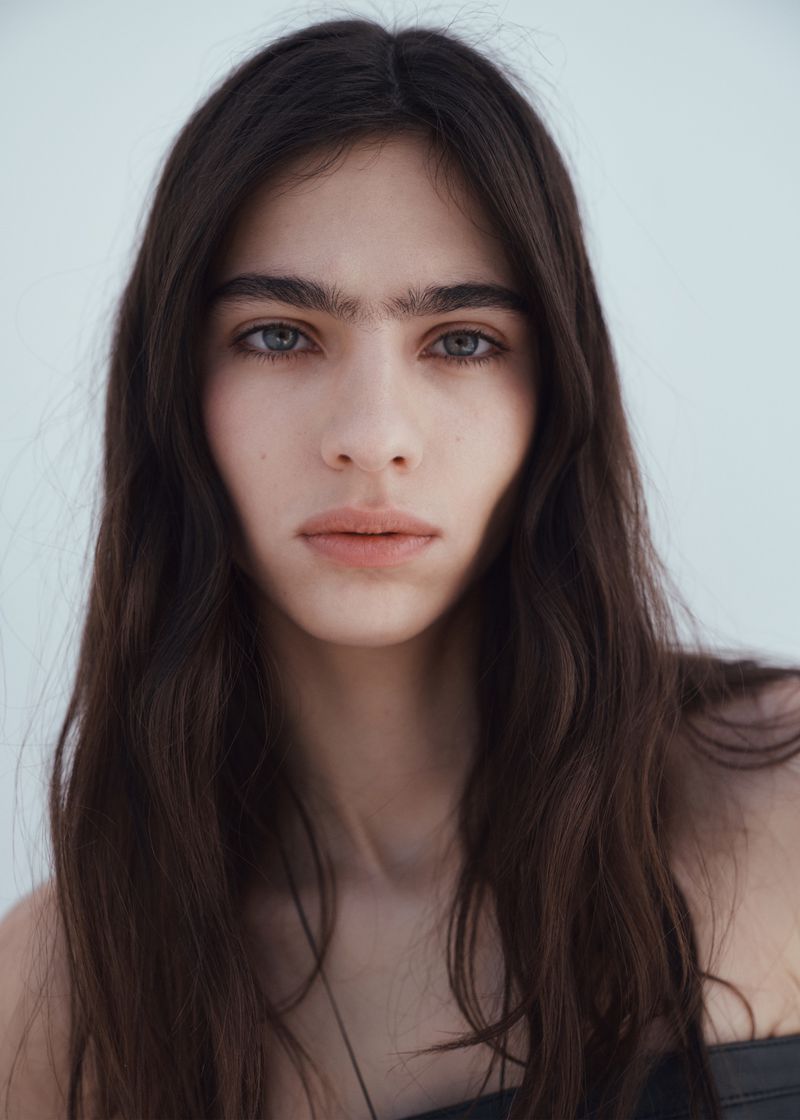 Close up portrait of model Loli Bahia with long dark hair and dark eyebrows against a light background for H and M S S 2026
