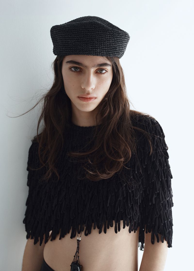 Model Loli Bahia wearing a dark beret and textured black top against a plain white background for H&M S/S 2026