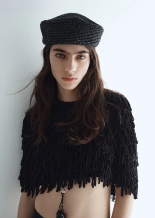 Model Loli Bahia wearing a dark beret and textured black top against a plain white background for H&M S/S 2026