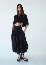 Model Loli Bahia in a black fringed crop top and loose skirt against a bright white background