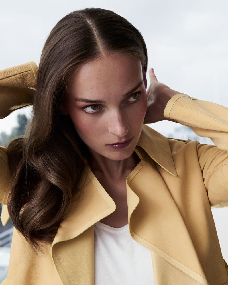 Woman wearing a yellow coat touching her hair in a beauty editorial portrait by Philip Gay