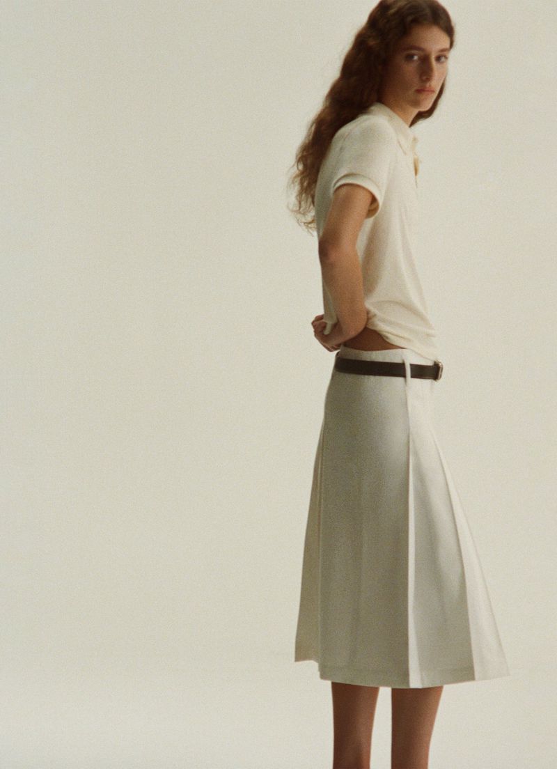 Model wearing a cream polo shirt and pleated skirt against a plain white background for the A.P.C. Spring Summer 2026 lookbook.