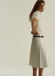 Model wearing a cream polo shirt and pleated skirt against a plain white background for the A.P.C. Spring Summer 2026 lookbook.