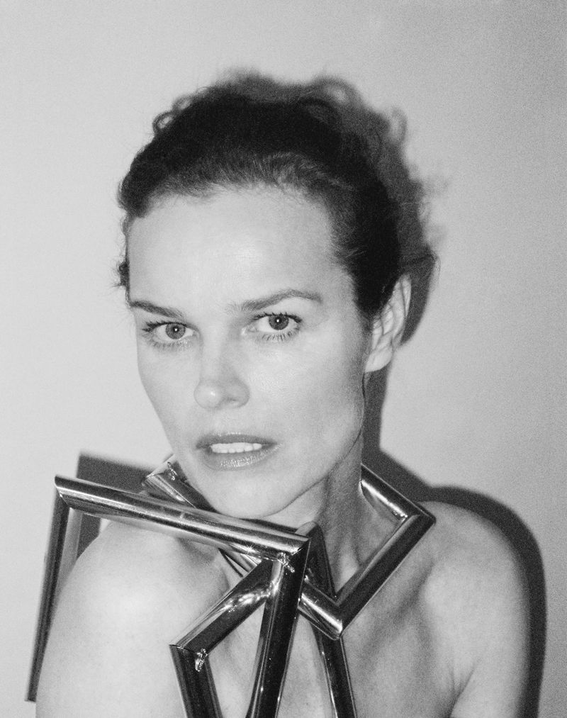 Monochrome portrait of a woman with curly hair wearing a metal geometric necklace against a plain background in a studio setting.