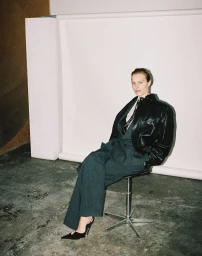 Eva Herzigova seated on a stool wearing a black leather jacket and grey trousers for CAP 74024