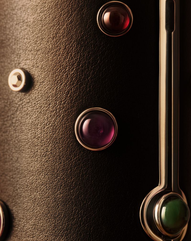 Macro shot of black textured leather surface embedded with polished cabochon gemstones in silver settings and a vertical metallic bar