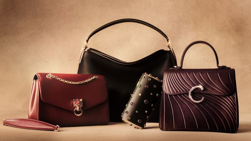 Collection of luxury leather handbags and a jewelled clutch arranged against a neutral textured studio background.