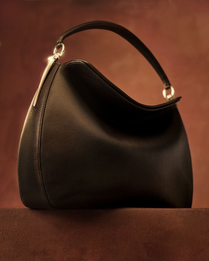 Black leather handbag with metal hardware resting on a brown surface against a warm textured background for Vogue.