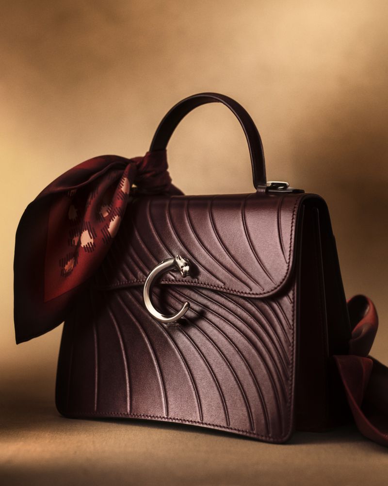 Burgundy leather handbag with curved detailing, a silver panther clasp, and a knotted scarf draped on the handle, studio lit.
