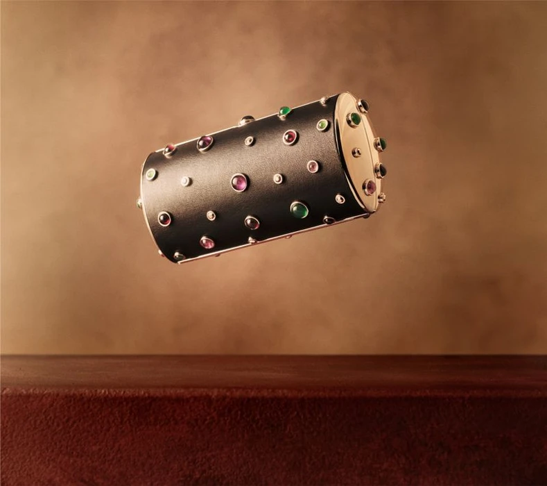 A cylindrical jeweled luxury case floats above a dark red wooden surface against a textured brown background.
