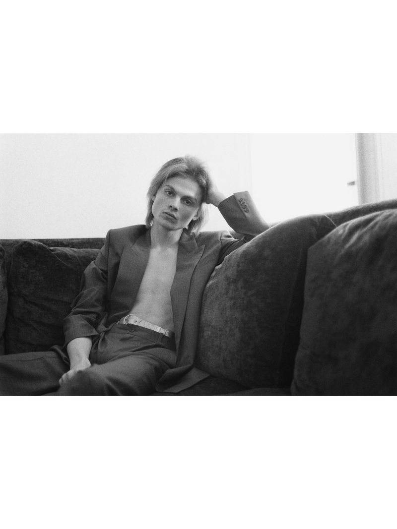 Young man in an open suit jacket seated on a dark sofa for Crosscurrent A room with a view project