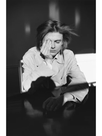 Monochrome portrait of a young man sitting at a table with his hand covering his face