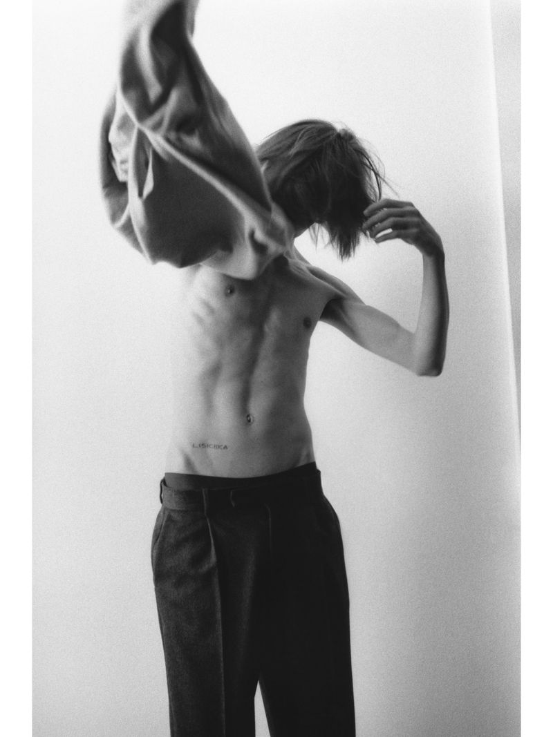 Monochrome portrait of a person pulling off a shirt against a plain light background