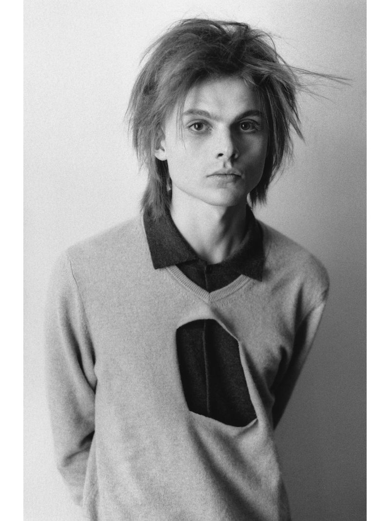 Monochrome portrait of a young man wearing a cutout sweater against a plain background