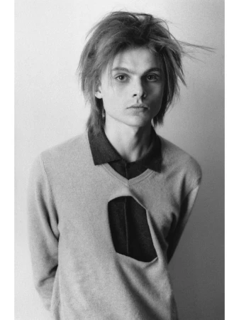 Monochrome portrait of a young man wearing a cutout sweater against a plain background