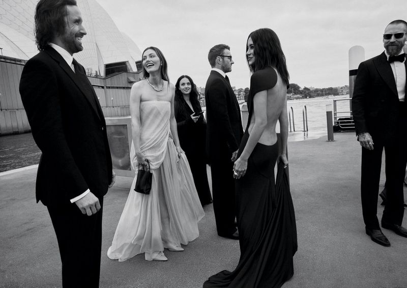 Monochrome editorial photo of formal guests gathered on a pier with the Sydney Opera House visible in the background.