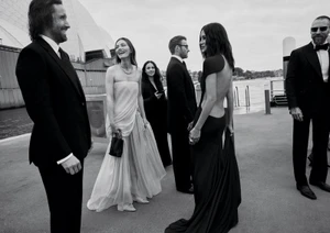 Monochrome editorial photo of formal guests gathered on a pier with the Sydney Opera House visible in the background.