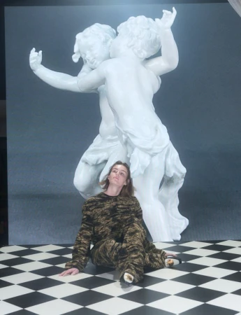 Model seated on a black and white checkerboard floor in front of a large white statue for Pop Magazine