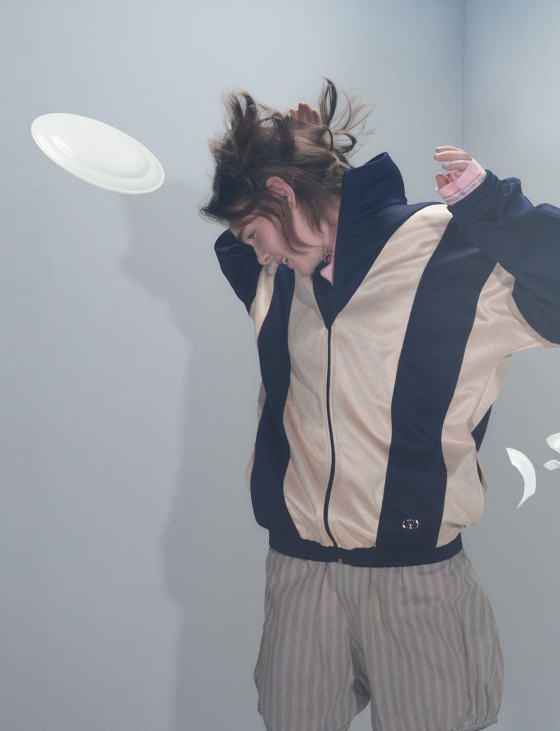 Model in a color-blocked zip jacket ducking under a flying white disc in a Pop Magazine editorial.