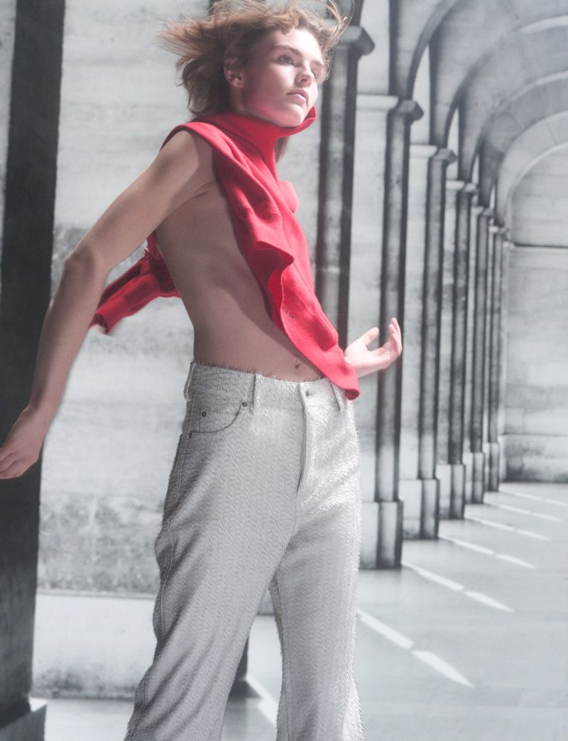 Model in red top and light grey trousers posing outdoors within a stone colonnade for Pop Magazine 54