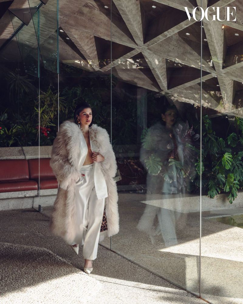 Ines Trocchia in a fluffy coat and white suit walking past glass reflection in Los Angeles architecture for Vogue China