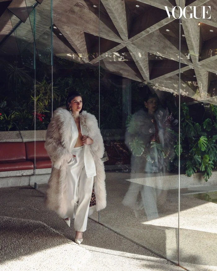 Ines Trocchia in a fluffy coat and white suit walking past glass reflection in Los Angeles architecture for Vogue China