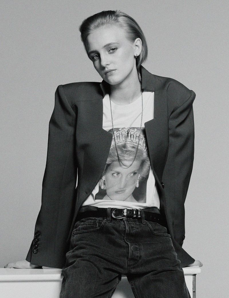Monochrome portrait of a model in a dark structured blazer and graphic t-shirt against a grey background