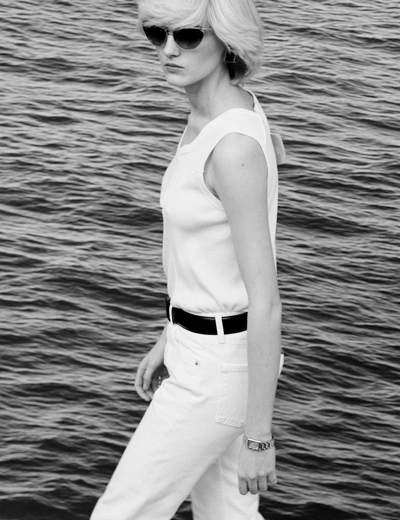 Model in white tank top and trousers wearing sunglasses standing by rippling water in Pop Magazine editorial