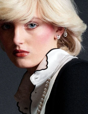 Close-up portrait of a blonde model wearing a white shirt with black trim, pearl necklace, and diamond earrings against a dark background.