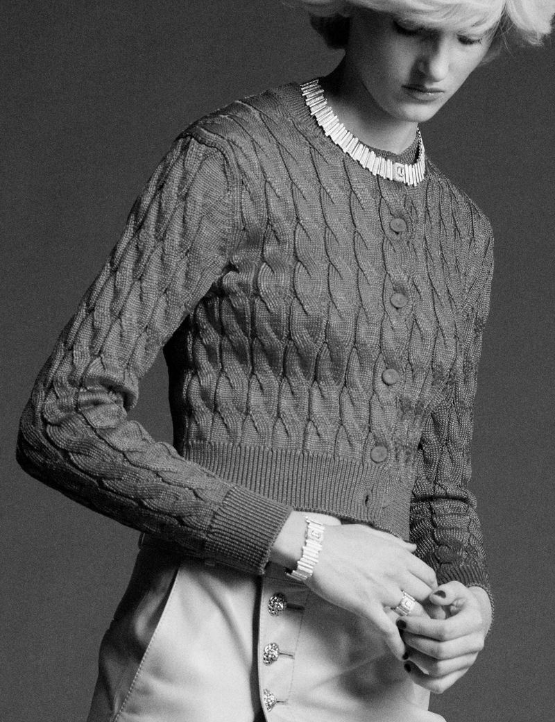 Model wearing a cable knit cardigan and light trousers against a grey backdrop for Pop Magazine