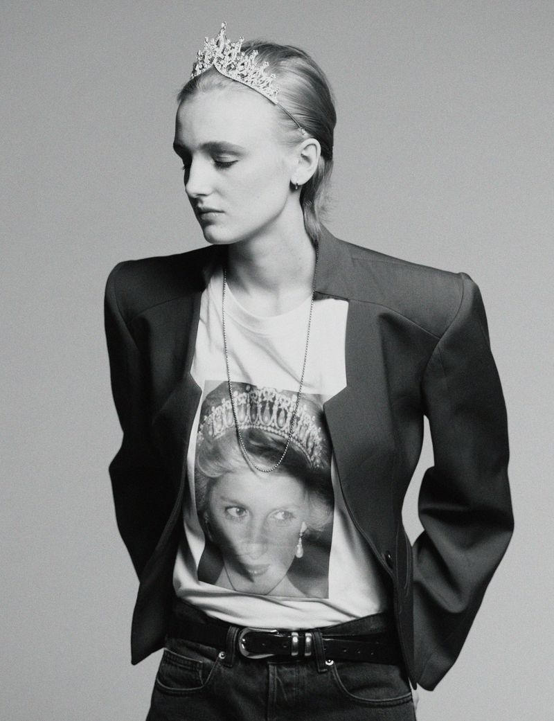 Monochrome portrait of a model wearing a tiara and graphic t-shirt under a structured blazer against a grey backdrop