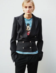 Model wearing a structured black blazer over a striped character t-shirt against a plain white background.