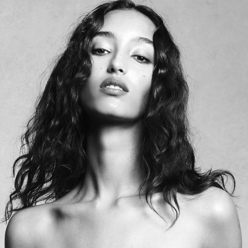 Close-up monochrome portrait of model Mona Tougaard featuring long dark wavy hair against a seamless background.