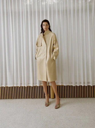 Nora Attal wearing a cream leather coat and heels standing before white curtains for Nour Hammour Spring Summer 26