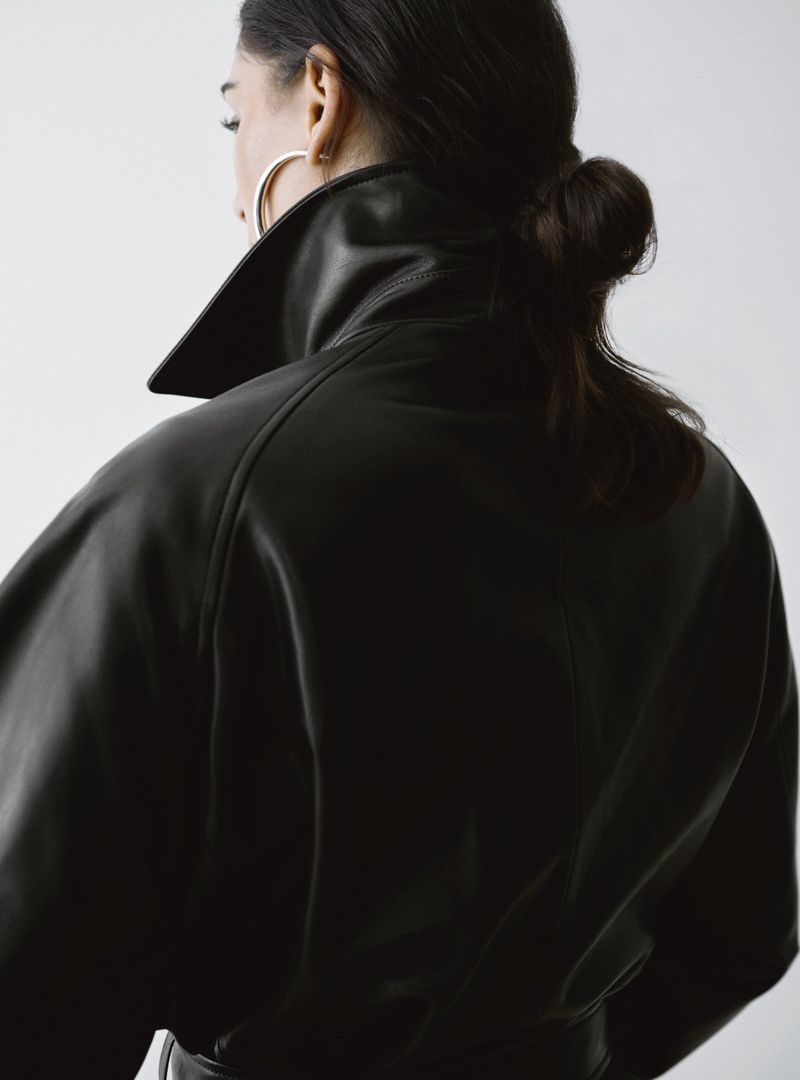 Model Nora Attal wearing a black leather coat with a high collar against a clean white studio background