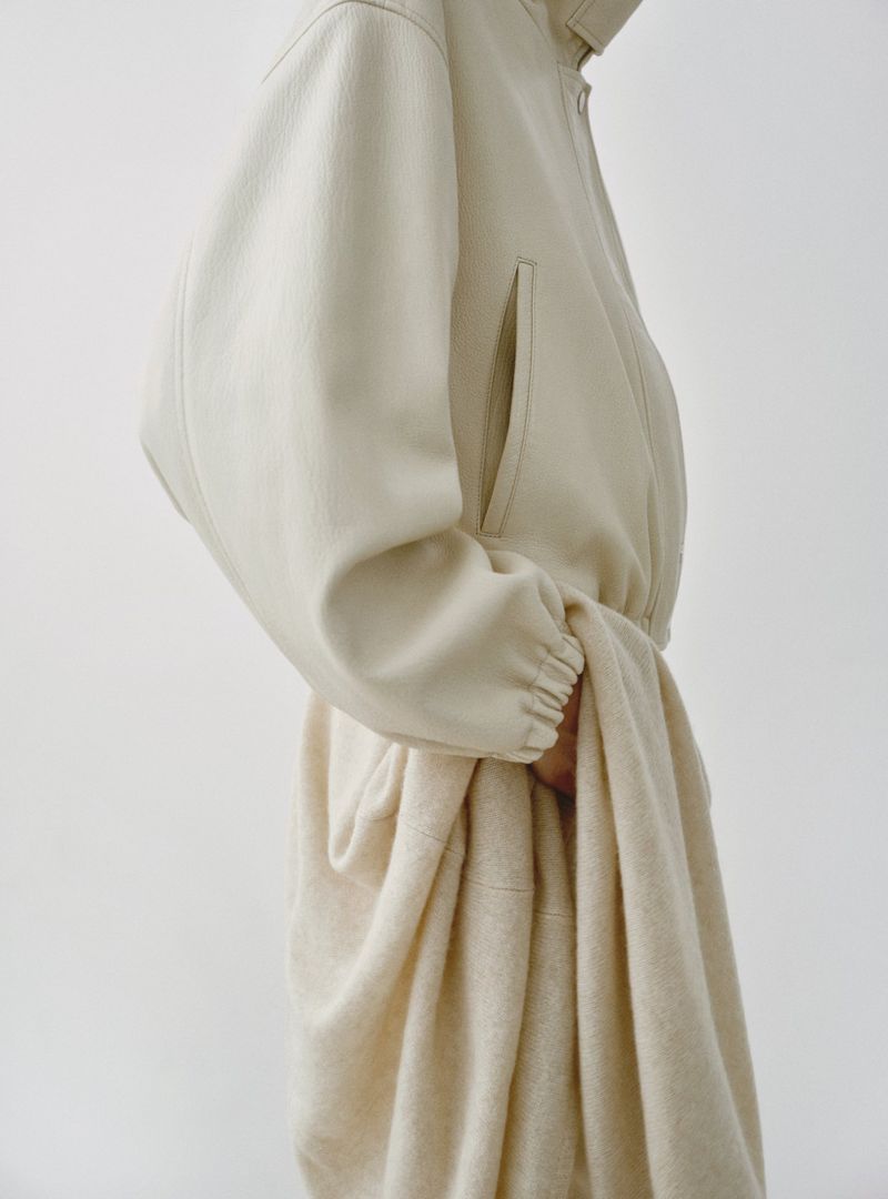 Model wearing a cream-colored textured coat against a plain white seamless studio background.