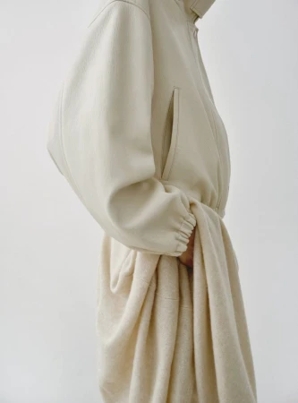 Model wearing a cream-colored textured coat against a plain white seamless studio background.